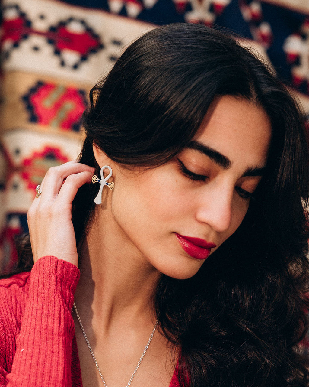 Woman adjusting an earring against a patterned background, sterling silver and 18k gold plated lotus, Ankh symbol earrings representing eternal life with a hammered texture and polished edges