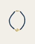 Glema teal bracelet with deep teal blue textured beads and a signature gold centerpiece holding a white pearl.