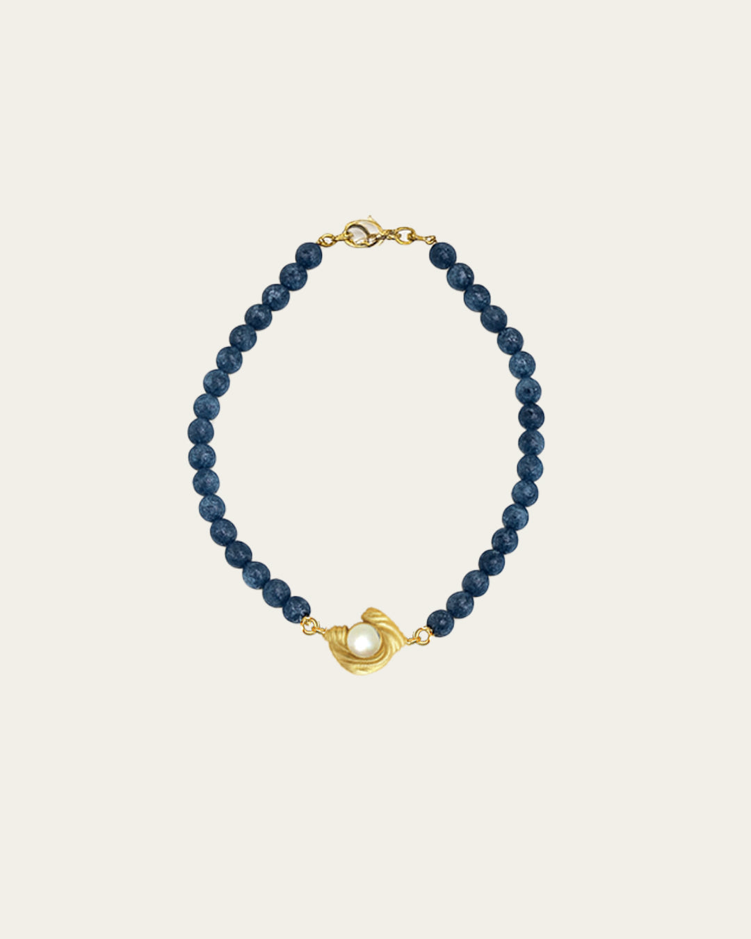 Glema teal bracelet with deep teal blue textured beads and a signature gold centerpiece holding a white pearl.