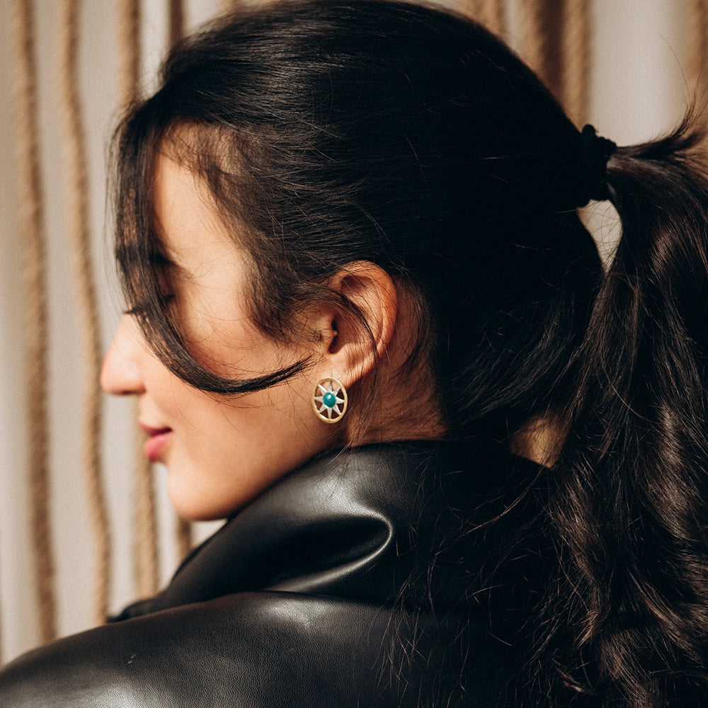 Woman with a ponytail wearing a black leather outfit and Ancient Sun gold drop earrings with a radiant sunburst design and central textured disk