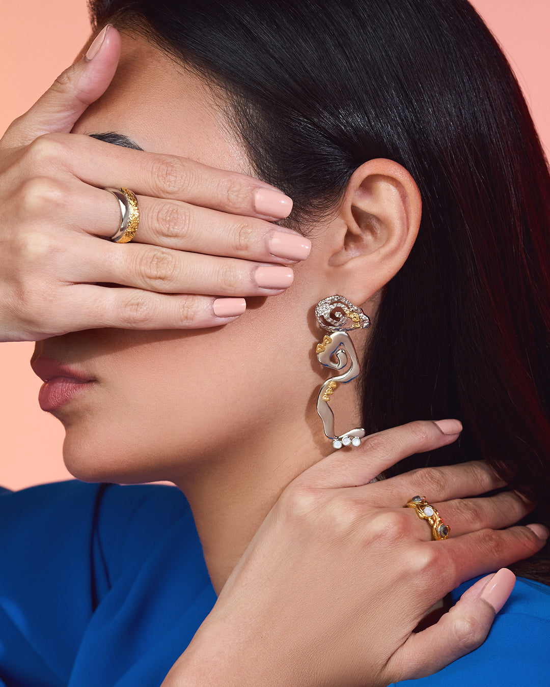 Close-up of a woman wearing Statement Cascade drop earrings in 18k gold plated metal with a fluid, liquid-gold waterfall silhouette