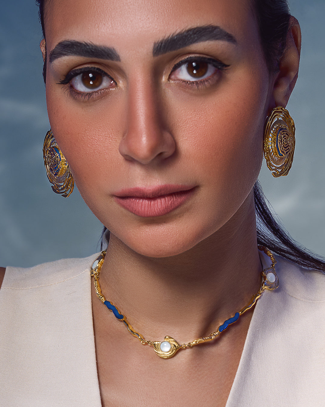 Glema necklace featuring earth-toned blue resin and a central textured gold charm with a paua seahell